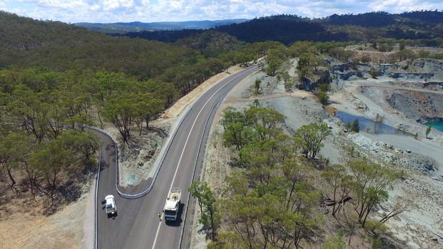 Aerial view of forked road wtih two trucks on it, surrounded by hills and vegetation