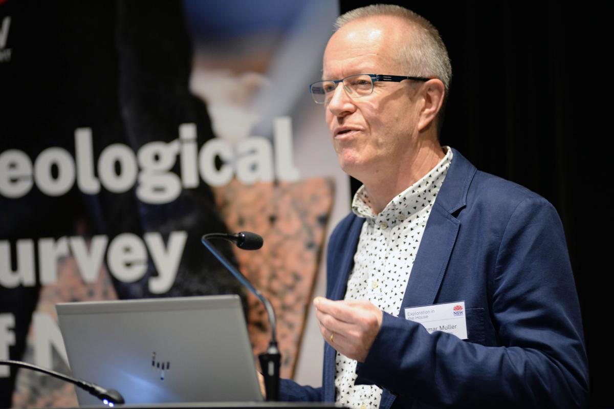 Cropped image of male presenter at lecturn addressing audience.